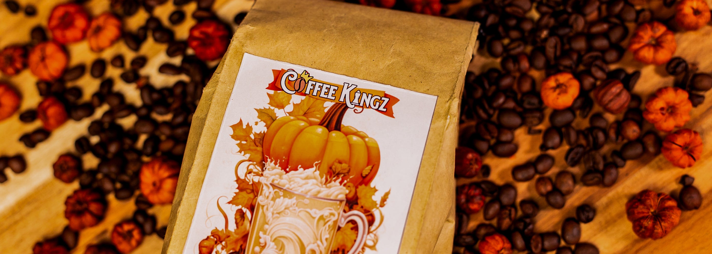 A package of Coffee Kingz pumpkin spice flavored coffee surrounded by a bed of coffee beans and autumnal accents, evoking cozy fall vibes.