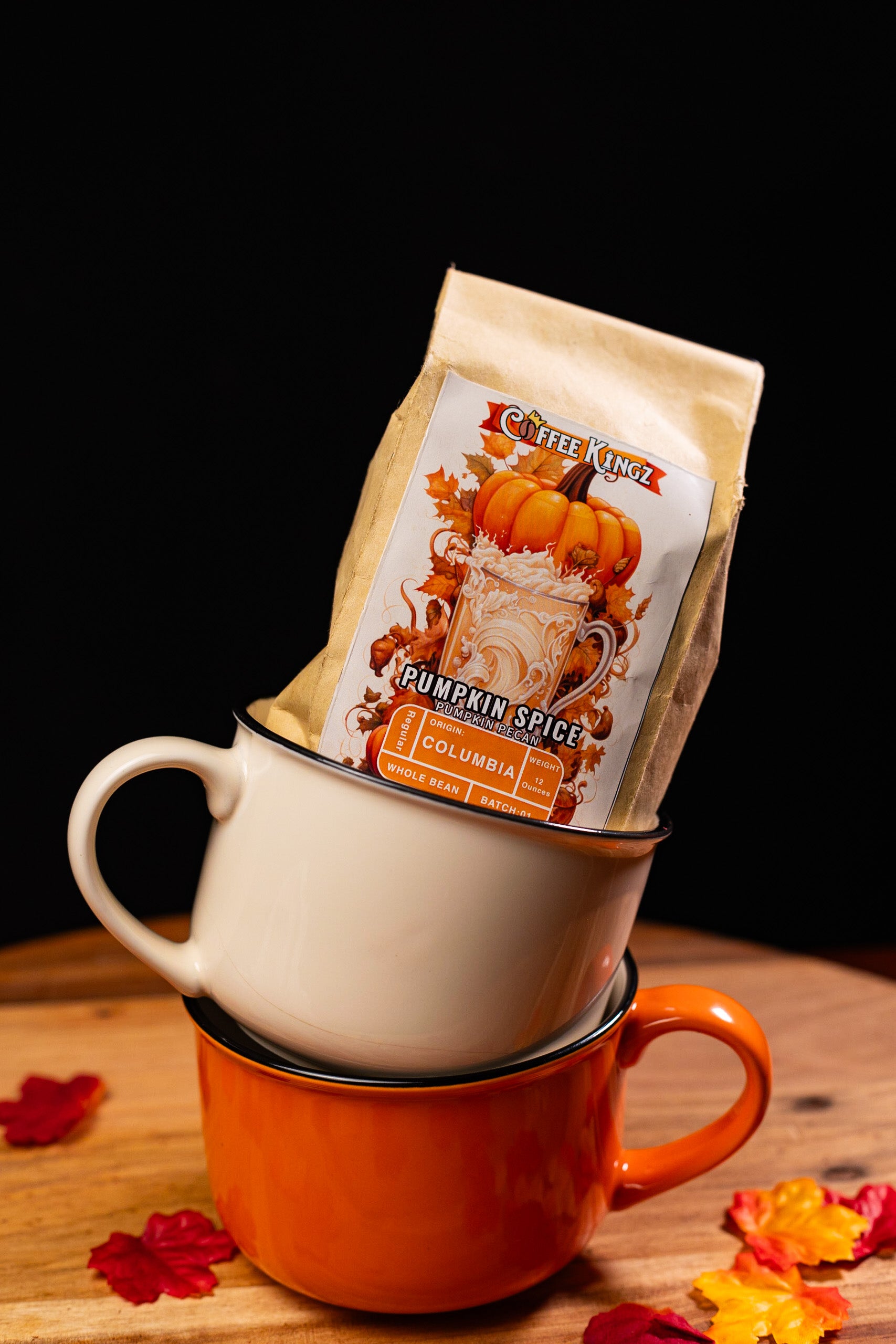 A bag of pumpkin spice flavored coffee kingz coffee beans perched on top of a stack of two coffee cups, with a warm, autumnal backdrop and scattered leaves.