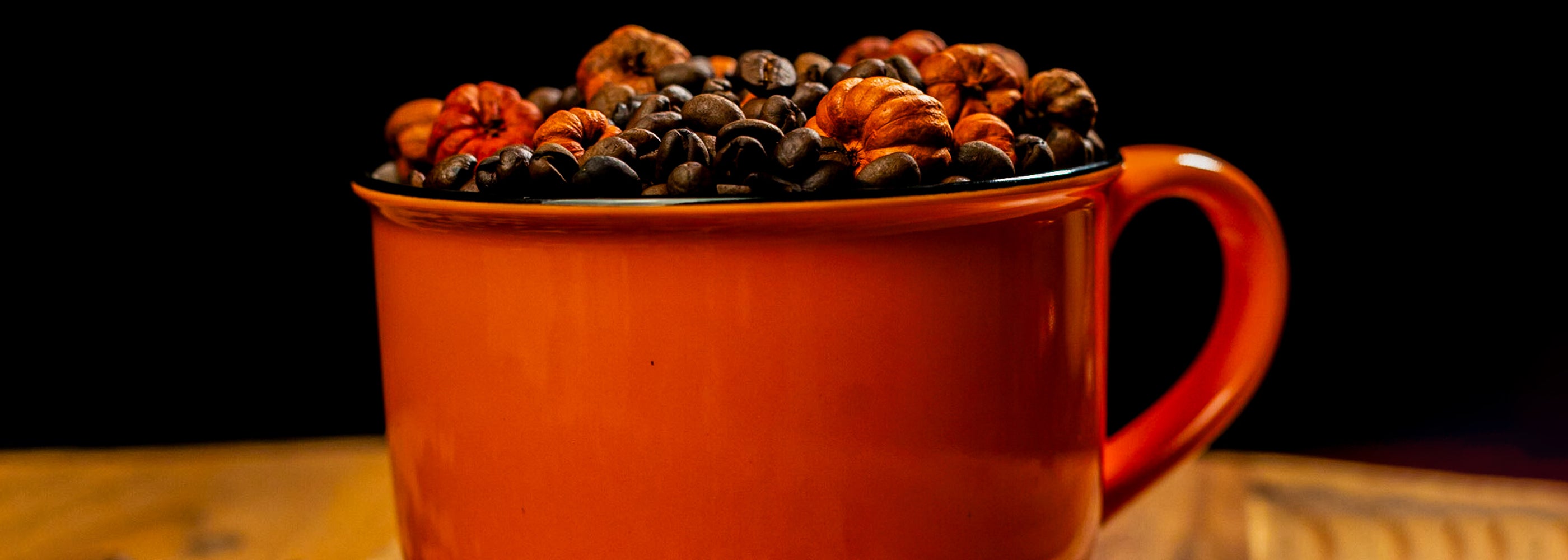 A full cup of coffee kingz beans with some beans spilling over the brim, against a dark background.