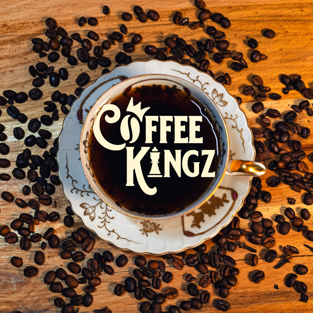 A royal brew: a classic porcelain cup filled with rich, dark coffee, crowned with a "coffee kingz" foam art, surrounded by a kingdom of scattered coffee beans on a wooden surface.